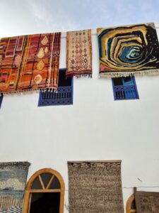 Cosa tur Marrakech. Fargerike berbertepper henger på hvit vegg i en riad. Oransje, blå og gule tepper.