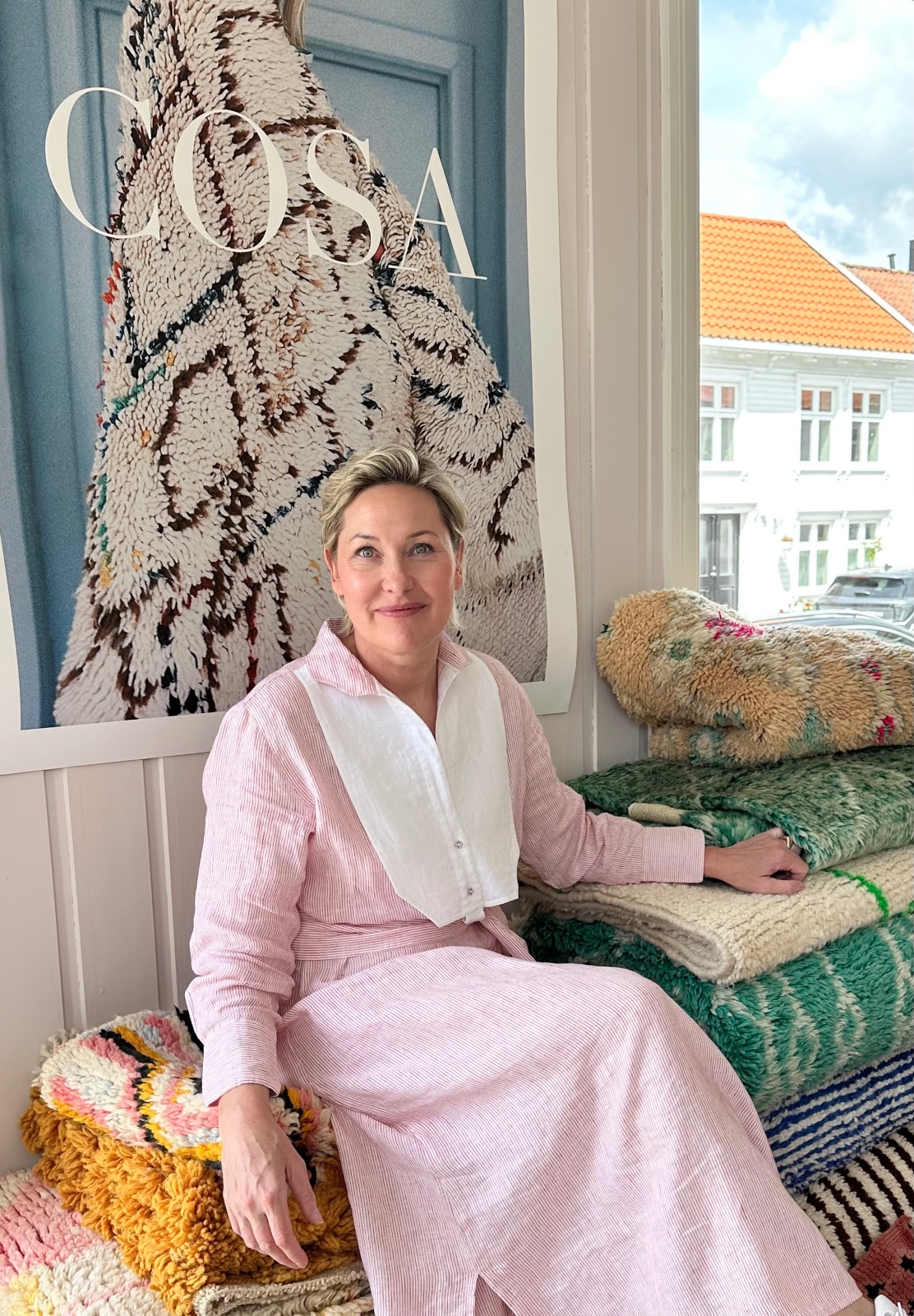 Hege, grunnlegger av Cosa, sitter på etablere marokkanske berbertepper i showroom, foran COSA-plakaten