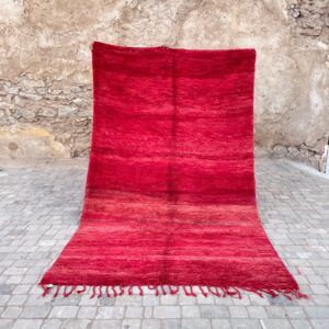 Et håndknyttet vintageteppe fra Marokko. Rød-rosa sjetteringer er gjennomgående gjennom hele teppet. Vist frem foran gamle bymurer i Marrakech