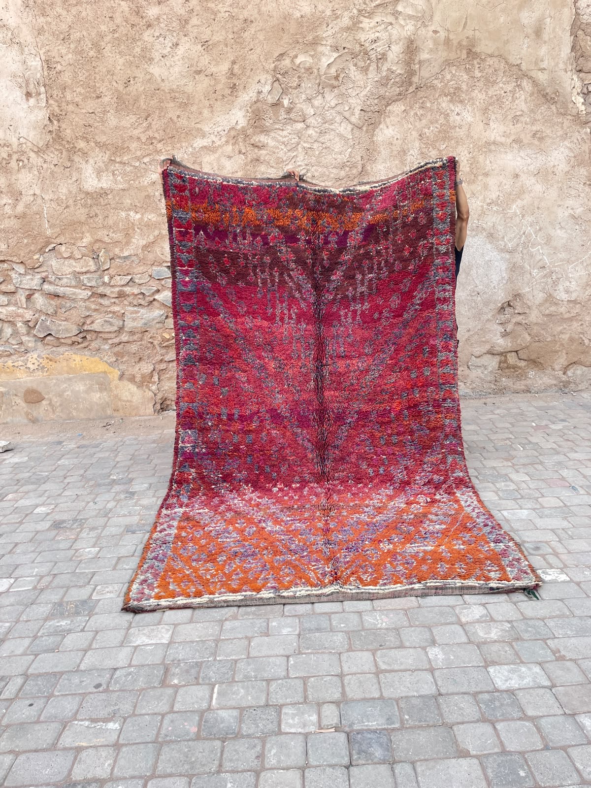 Et håndknyttet marokkansk vintageteppe fra Beni Mguild regionen i Marokko. Tykt og mykt, 100% naturlig ull. Lang lugg. Vist frem foran gamle bymurer i Marrakech
