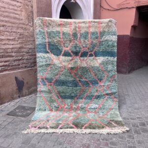 Håndknyttet marokkansk berberteppe med høy luv i salviegrønn og petrol, med korallrosa asymmetriske linjer, fotografert i en gate i Marrakech
