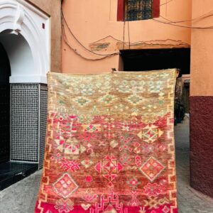 Vintage Boujaad-teppe fra Marokko, ca. 1970, i fargeforløp fra beige til rust og bringebærrosa med diamant- og korsmotiver, fotografert i en smug i Marrakech