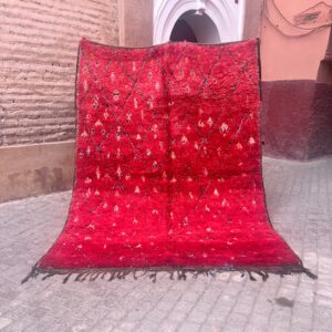 Rødt vintage marokkansk berberteppe med høy luv, mørkt diamantmønster og små hvite og oransje motiver, holdt opp i en gate i medinaen i Marrakech