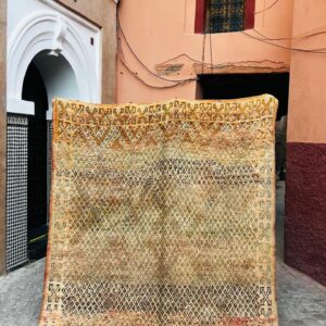 Vintage Beni Mguild-teppe fra Marokko, 1980-tallet, 272 x 200 cm, i oker og safran med tett brunt diamantmønster og X-motiver langs kantene, fotografert i en smug i Marrakech